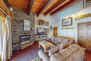 Ein gemütliches Wohnzimmer mit Kamin aus Stein, Holzbalken, einem Fernseher und einem Sofa.