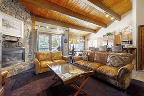 Ein gemütliches Wohnzimmer mit Kamin aus Stein, Ledersofas, einem Glastisch und Holzbalken an der Decke.