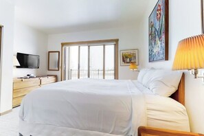 Ein Hotelzimmer mit einem großen Bett, einem Fernseher, einer Holzkommode, einem Fenster mit Blick und einem Gemälde an der Wand.