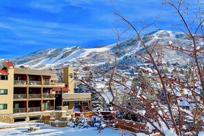 Ein mehrstöckiges Hotel mit Balkonen, im Hintergrund eine Skipiste und schneebedeckte Bäume.