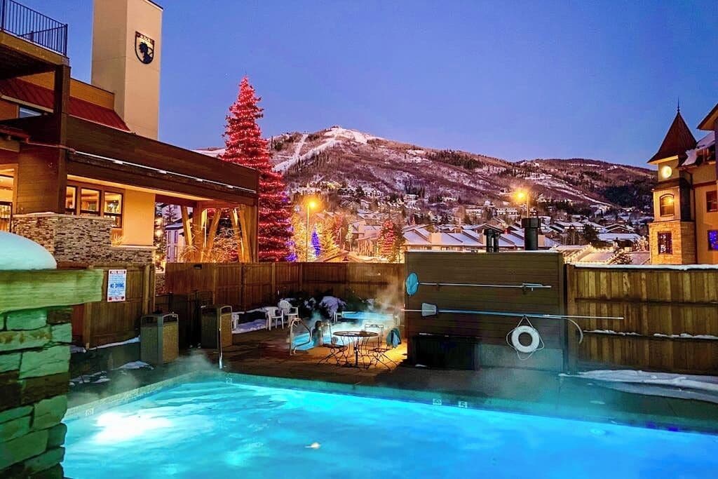 A pool area with a hot tub, outdoor seating, and a view of a snowy mountain.