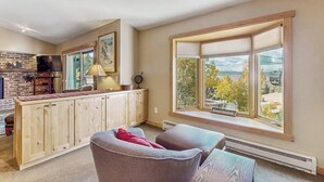 Uma sala de estar aconchegante com lareira, uma janela grande com persianas e vista para árvores.