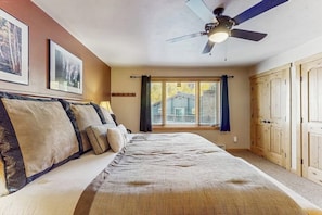 Ein Schlafzimmer mit einem Bett, Deckenventilator, einem Fenster mit Vorhängen und Holztüren.