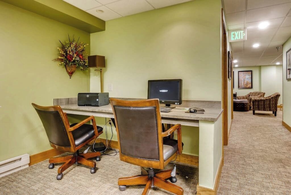 A conference room with two office chairs, a desk with a computer, and a decorative plant.