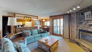 Ein Wohnzimmer mit Sofa, Couchtisch, Kamin und einer Küche im Hintergrund.