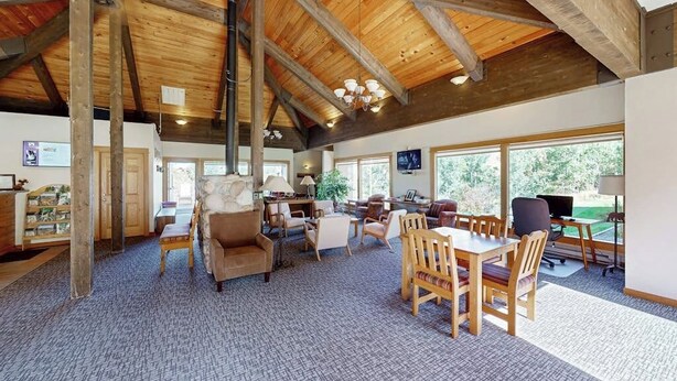 Una habitación amplia con un techo alto de madera, una chimenea, una zona de comedor y ventanas grandes.
