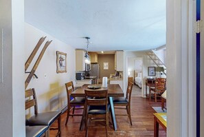 Ein Essbereich mit Holztisch und Stühlen, im Hintergrund eine Küche und eine Treppe, die in eine andere Ebene führt.