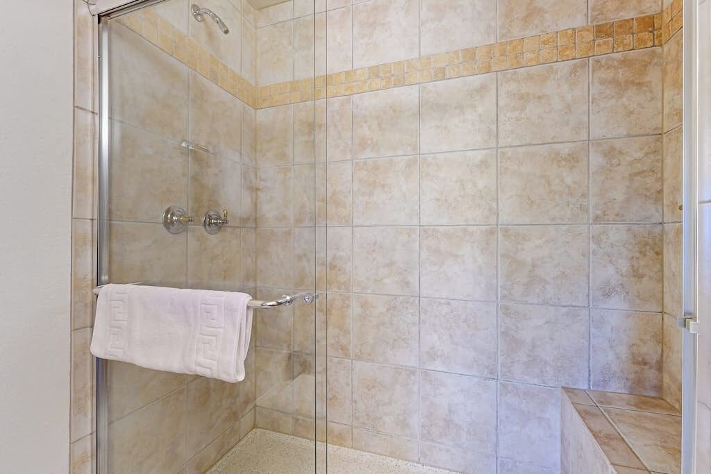Une douche fermée par des parois en verre, avec des carreaux de couleur beige, un porte-serviettes et un panneau de commande.