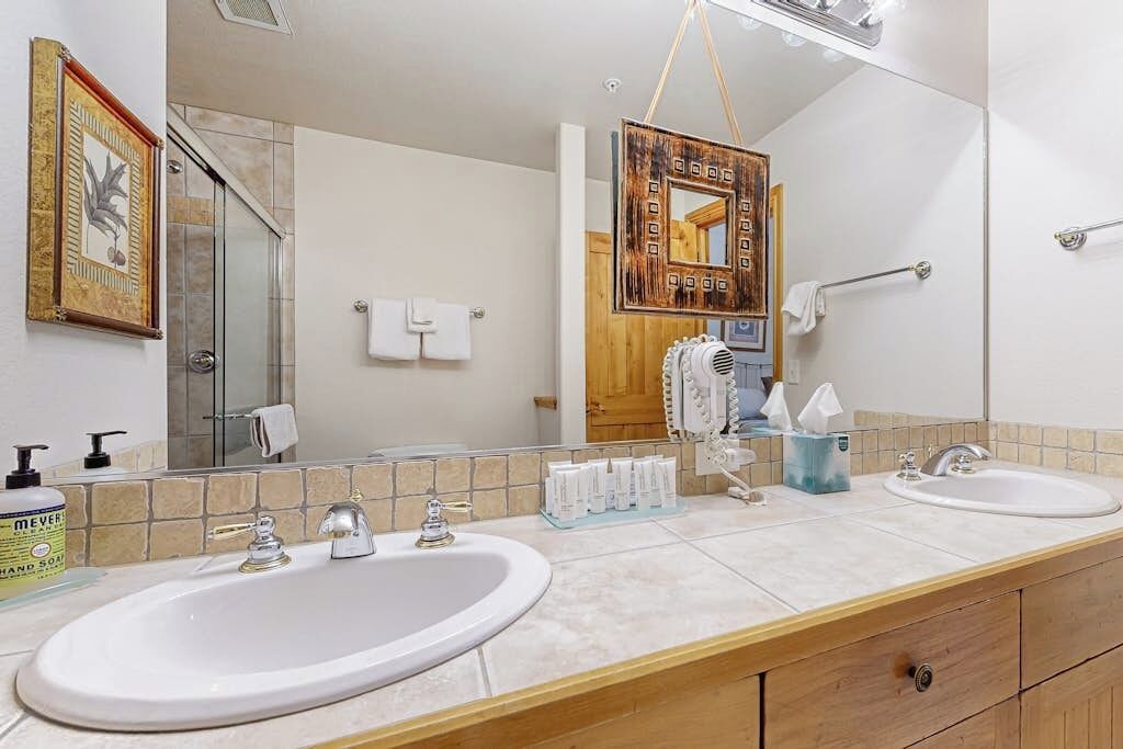 A bathroom with two sinks, a large mirror, a towel rack, and a shower area.