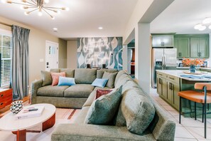 Ein modernes Wohnzimmer mit Ecksofa, Couchtisch und Küchenbereich mit grünen Schränken sowie einem Edelstahl-Kühlschrank.