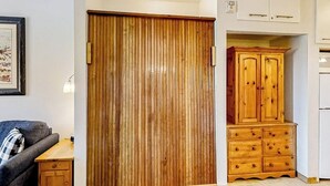 A room with a wooden wardrobe, a wooden cabinet with drawers, a small table, and a framed picture on the wall. - Base area studio w/shared pool & hot tub, private balcony - steps from ski lifts (Steamboat Springs)