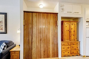 Ein Zimmer mit Holzschrank, einer Kommode mit Schubladen, einem kleinen Tisch und einem gerahmten Bild an der Wand.