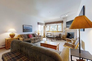 A living room with a sofa, armchairs, a coffee table, a fireplace, and a television. - Large condo just steps from the gondola & base area w/ shared pool & hot tub (Steamboat Springs)