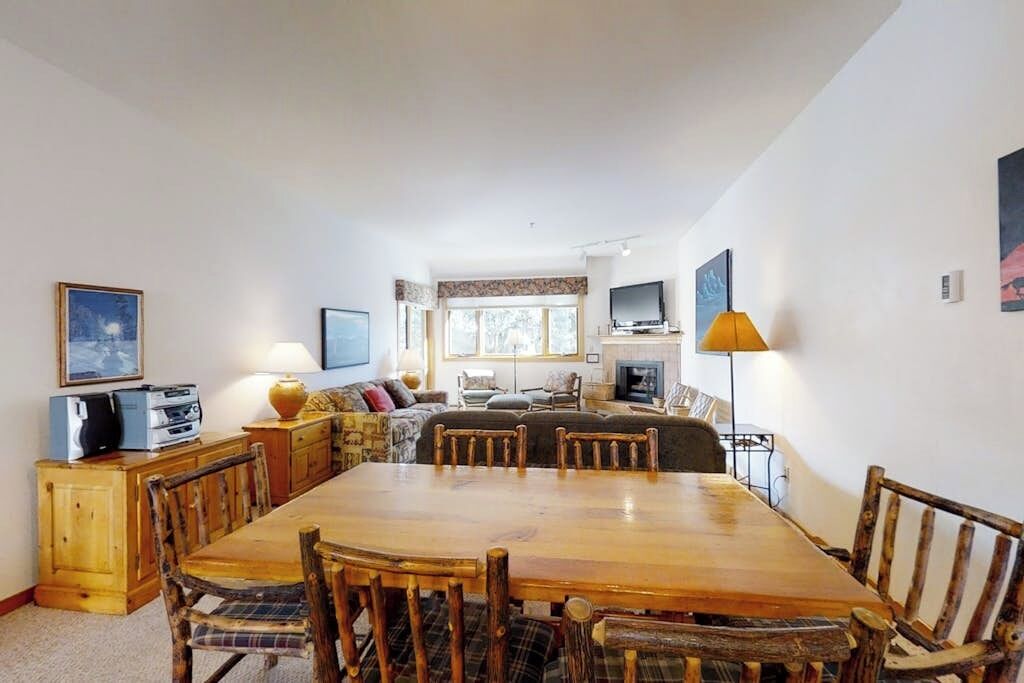 A dining area with a wooden table and chairs, a sofa set, a television, and a lamp.