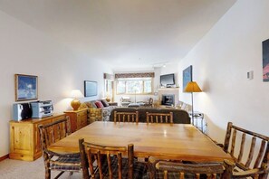 A dining area with a wooden table and chairs, a sofa set, a television, and a lamp. - Large condo just steps from the gondola & base area w/ shared pool & hot tub (Steamboat Springs)