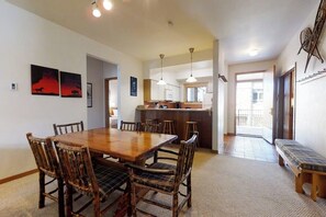 A dining area with a wooden table and chairs, a kitchen in the background, and a bench by the door. - Large condo just steps from the gondola & base area w/ shared pool & hot tub (Steamboat Springs)