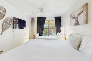 Ein Hotelzimmer mit Bett, Deckenventilator, Fernseher und einem fenster mit Vorhängen.