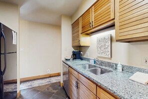 Eine Küche mit Granit-Arbeitsplatten, Holzschränken, einer Kaffeemaschine und einem an der Wand befestigten Schild.