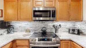 Una cocina con armarios de madera, microondas de acero inoxidable, estufa a gas y cafetera.
