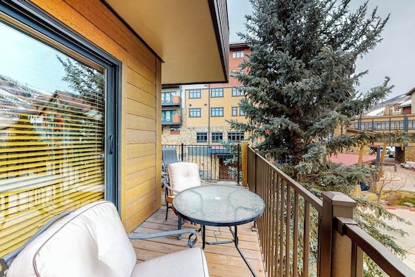 Ein Balkon mit Glastisch und Stühlen, Blick auf einen Baum und ein Gebäude im Hintergrund.