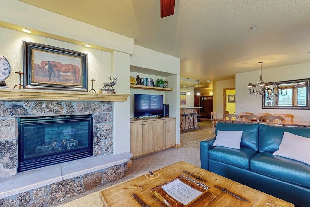 A living room with a stone fireplace, a television, a blue leather sofa, and a wooden coffee table.