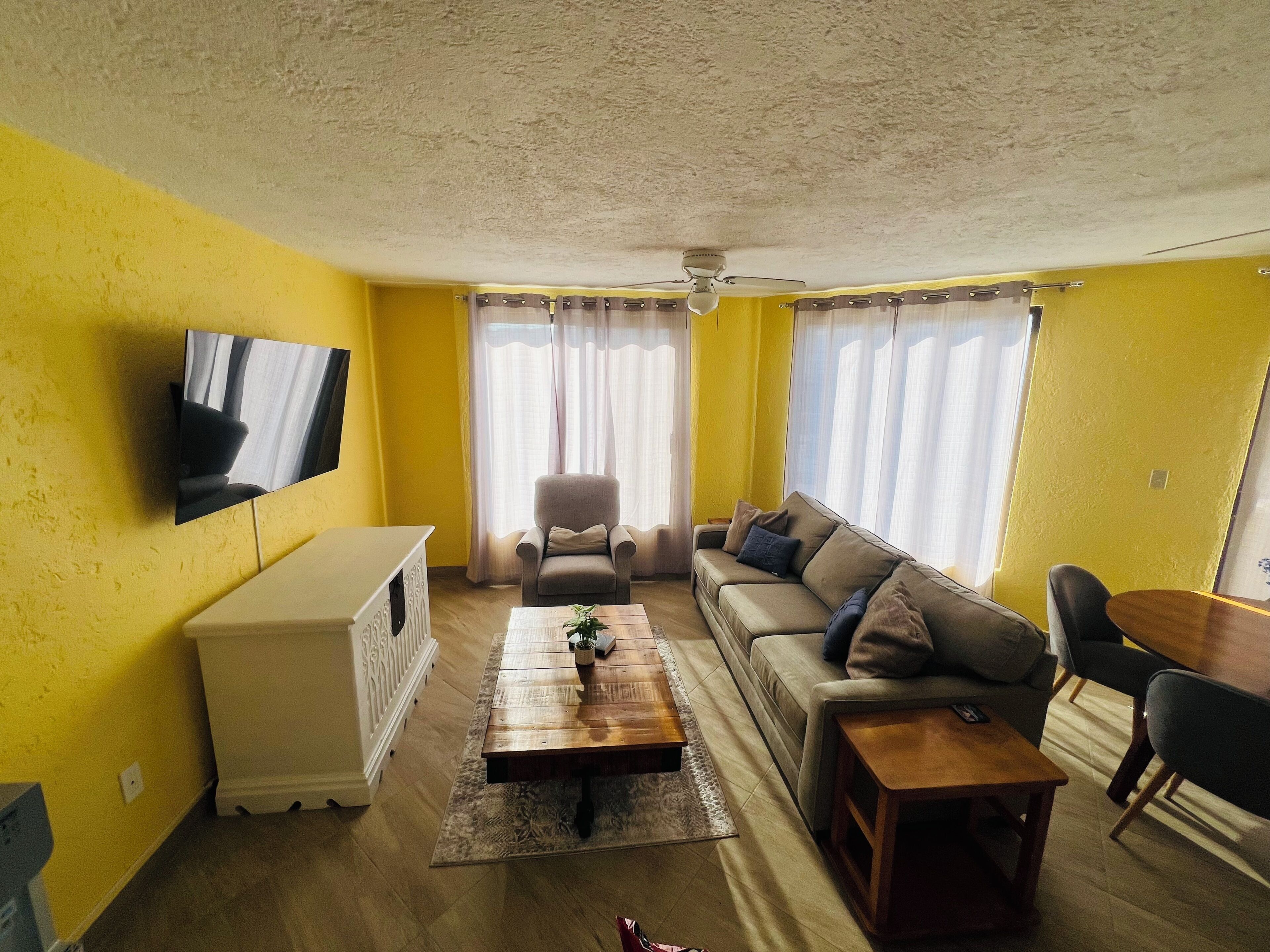 Ein Wohnzimmer mit Sofa, Sessel, Couchtisch, Fernseher und Vorhängen.