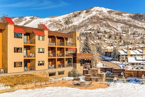 Ein mehrstöckiges Hotel mit Balkonen, im Hintergrund ein Ski-Hang und ein Poolbereich.