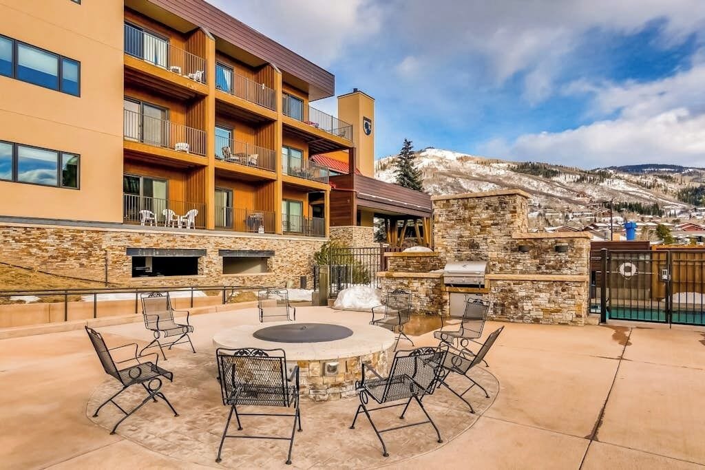 A hotel with a stone fireplace, outdoor seating, and a view of a snowy mountain.