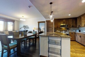 A modern kitchen with wooden cabinets, a central island, and a dining area with a table and chairs. - Stylish luxury condo w/gas fireplace, washer/dryer, shared pool, hot tubs, & gym (Steamboat Springs)