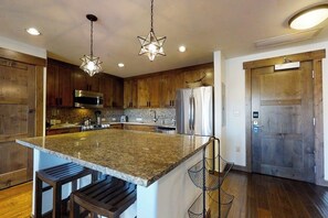 A kitchen with granite countertops, stainless steel appliances, wooden cabinets, and a central island with bar stools. - Stylish luxury condo w/gas fireplace, washer/dryer, shared pool, hot tubs, & gym (Steamboat Springs)