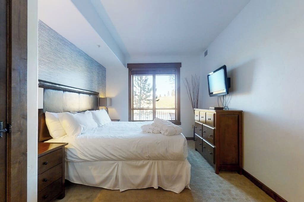 A bedroom with a bed, a television, a dresser, and a window.