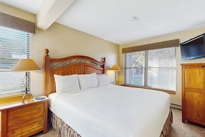 A hotel room with a large bed, two bedside tables, a TV, and windows with blinds. - Warm & inviting condo with sauna, pool & hot tubs (Steamboat Springs)