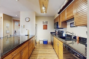A kitchen with wooden cabinets, a granite countertop, a microwave, and a dishwasher. - Warm & inviting condo with sauna, pool & hot tubs (Steamboat Springs)