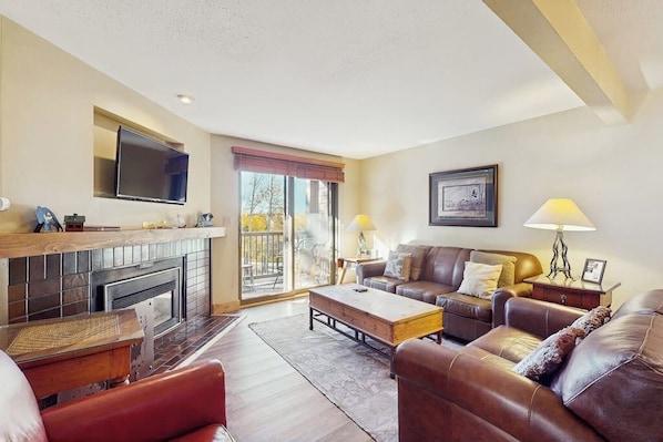 A living room with a fireplace, leather sofa, and a flat-screen TV. - Warm & inviting condo with sauna, pool & hot tubs (Steamboat Springs)