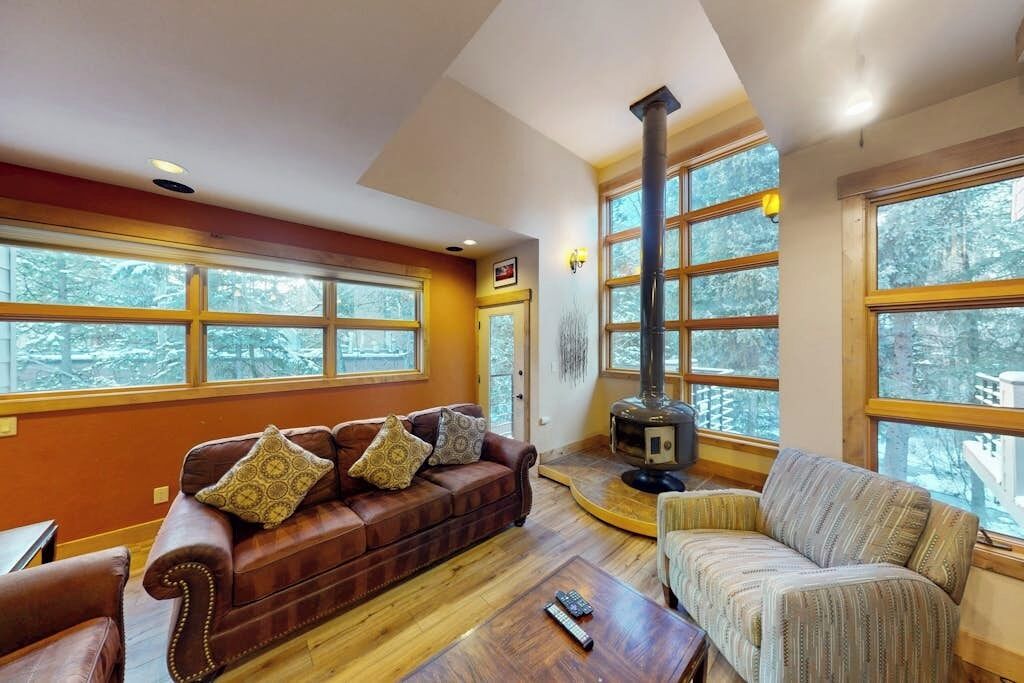 A cozy living room with a fireplace, large windows, and a brown leather sofa.