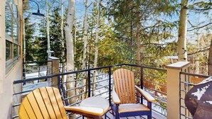 A balcony with two Adirondack chairs, a metal railing, and a view of tall trees. - Modern Frisco Townhome with upscale features & world-class skiing (Frisco)