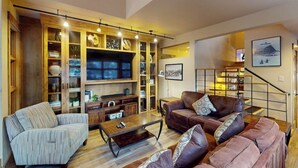 A living room with a sofa, armchair, coffee table, TV, and built-in shelving with decorative items. - Modern Frisco Townhome with upscale features & world-class skiing (Frisco)