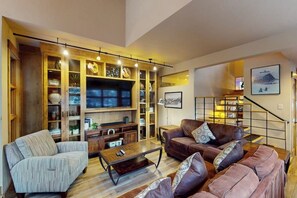 Una sala de estar con sofá, sillón, mesa de centro, televisor y estanterías empotradas decoradas con objetos decorativos.