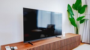 Ein Flachbildfernseher auf einem Holz-TV-Schrank, zusammen mit einer Fernbedienung und einem Smartphone.