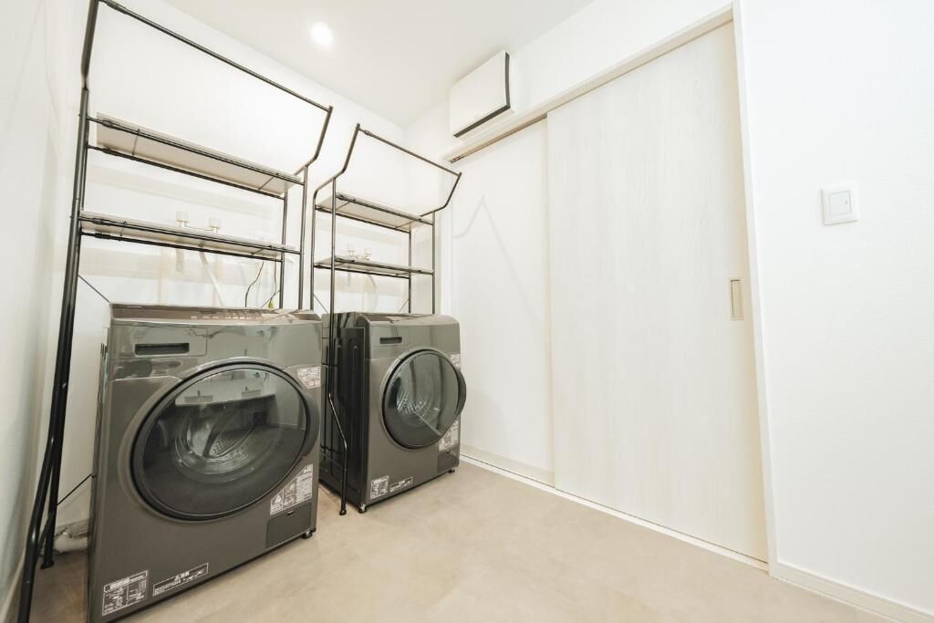 A laundry room with two front-loading washers and dryers, a white wall, and a door.