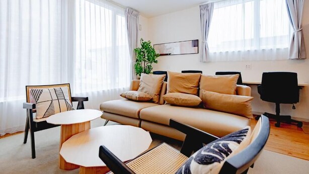 Ein modernes Wohnzimmer mit einer Couch, einem runden Tisch und einem Sessel. Eine Pflanze, ein gerahmtes Bild an der Wand und ein Fernseher sind ebenfalls vorhanden.