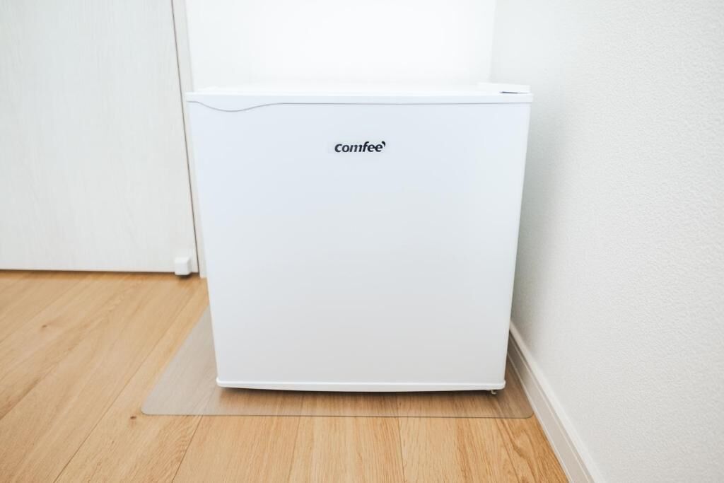 Een witte, draagbare koelkast met het merk 'comfee' in een hoek van een kamer met houten vloeren en witte muren.