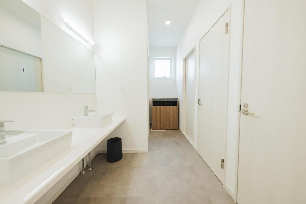 A modern bathroom with two sinks, a mirror, and a trash bin.