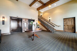 Eine Lobby mit einem gemusterten Teppich, einem runden Holztisch, einem Aufzug, einer Treppe und einer Holztür.