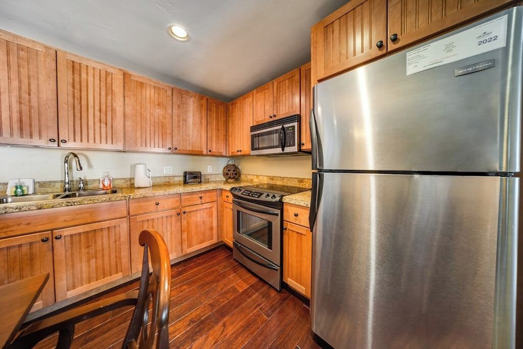 Una cocina con gabinetes de madera, un refrigerador de acero inoxidable, un microondas, un horno y un lavamanos.