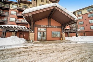 Ein Gebäude mit der Beschriftung 'BASE CAMP ONE', einem überdachten Eingang, steinernen Säulen und einem schneebedeckten Boden.