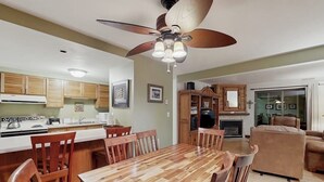 A dining area with a wooden table and chairs, a ceiling fan, and a kitchen in the background. - Timber Run 416 - Appealing condo with sauna, pool, hot tubs & barbecue area (Steamboat Springs)