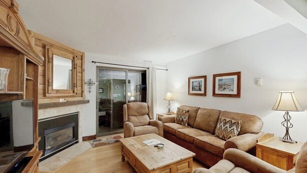 A living room with a fireplace, leather sofa, wooden coffee table, and a glass door leading to a balcony. - Timber Run 416 - Appealing condo with sauna, pool, hot tubs & barbecue area (Steamboat Springs)