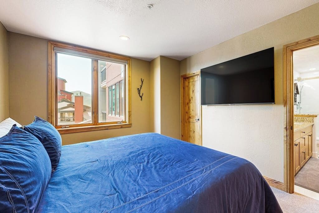 A bedroom with a bed, a window, a TV, and a door leading to a balcony.