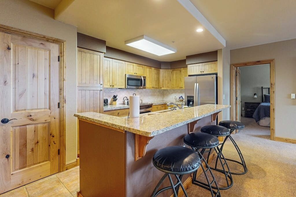 Une cuisine avec des meubles de rangement en bois, un îlot central doté de tabourets, un four à micro-ondes et un réfrigérateur.